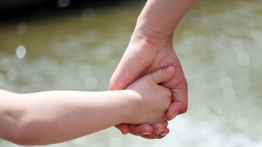 Eine Kinderhand liegt in der Hand einer erwachsenen Frau.