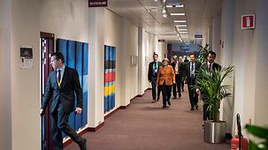 Chancellor Angela Merkel walks along a corridor with her delegation.