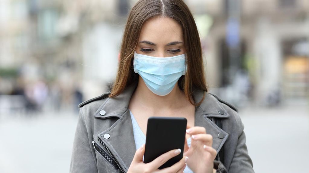 Junge Frau mit medizinischer Maske, die ein Smartphone in der Hand hält 