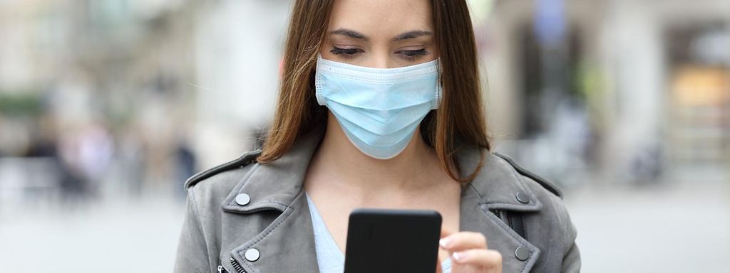 Junge Frau mit medizinischer Maske, die ein Smartphone in der Hand hält 