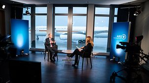 Bundeskanzler Olaf Scholz während eines Interviews mit Moderatorin Tina Hassel auf dem Flughafen. 