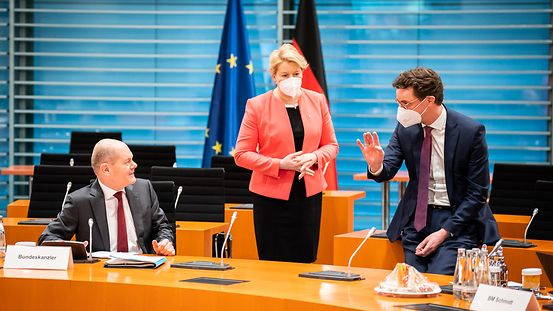 Das Bild zeigt Kanzler Scholz am Tisch sitzend im Gespräch mit der stehenden Regierenden Bürgermeisterin Giffey und dem an einem Tisch lehnenden NRW-Ministerpräsidenten Wüst.