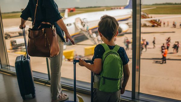 Foto eines kleinen Jungen und seiner Mutter am Flughafen. Beide schauen auf ein Flugzeug.