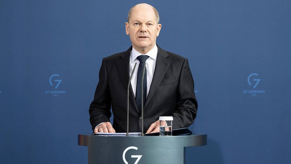Das Bild zeigt Bundeskanzler Olaf Scholz am Rednerpult im Kanzleramt stehend vor einer blauen Wand.