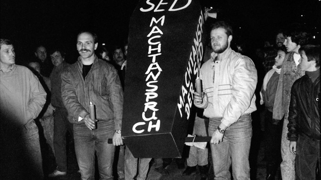 Demonstranten tragen während einer Demonstration symbolisch den Machtanspruch der SED zu Grabe.