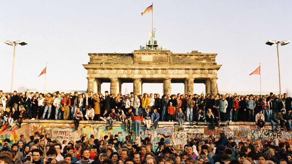Am 9. November 1989 öffnet die DDR ihre Grenze nach Westberlin und zur Bundesrepublik; nach 28 Jahren fällt die Mauer. Bewohner aus West- und Ostberlin stehen am 10.11.89 auf der Mauerkrone am Brandenburger Tor.