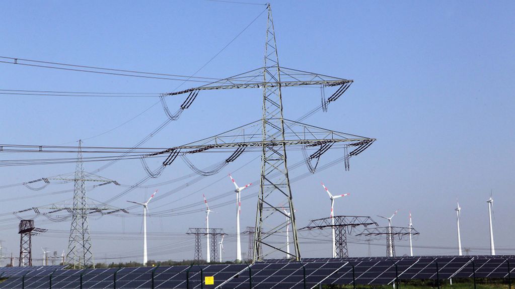 Strommasten und Windkrafträder stehen bei Nauen (Brandenburg) hinter einem Solarpark. Strom, Strommasten, Solarenergie, Windenergie, Windkraftanlagen