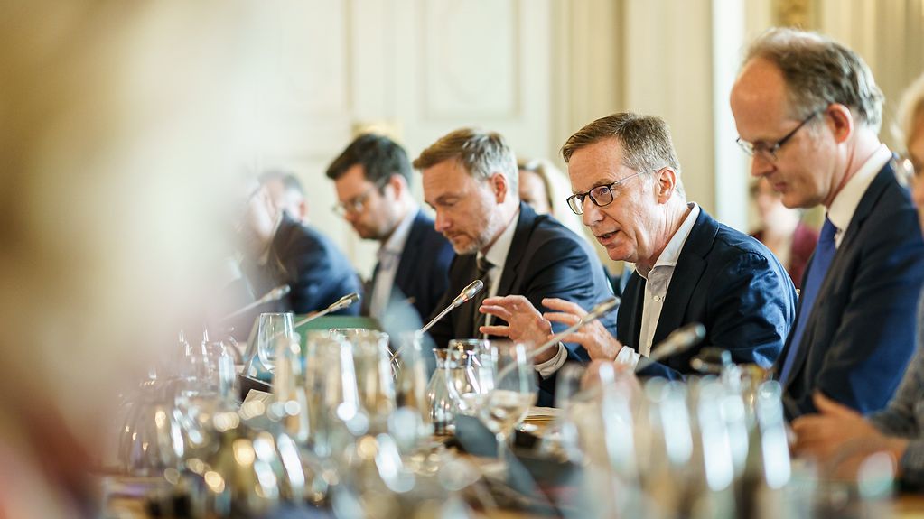 Michael Hüther, Direktor des Instituts der Deutschen Wirtschaft, und Sebastian Dullien, Direktor des Instituts für Makroökonomie und Konjunkturforschung, sitzen mit am Sitzungstisch bei der Klausur in Meseberg.