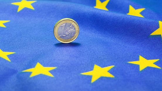 Eine Euro-Münze auf einer EU-Fahne.