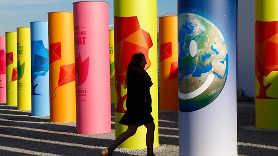 Frau läuft zwischen bunten Säulen durch, auf denen für die UN-Klimakonferenz geworben wird.