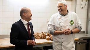 Bundeskanzler Scholz steht neben einem Bäckermeister, beide lachen