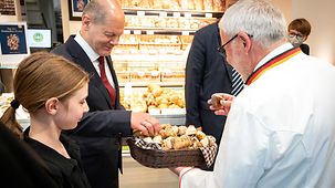 Bundeskanzler Scholz greift in einem kleinen Brotkorb, in einer Bäckerei