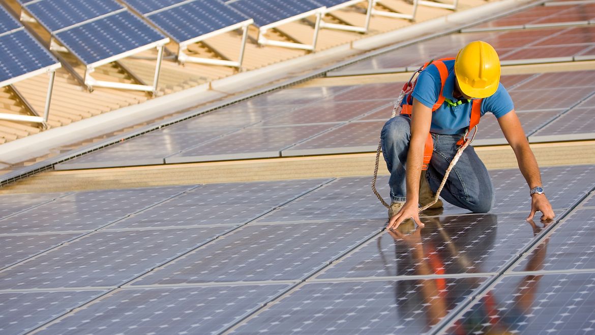 Ein Bauarbeiter mit Helm montiert Solarpanels auf einem Dach.