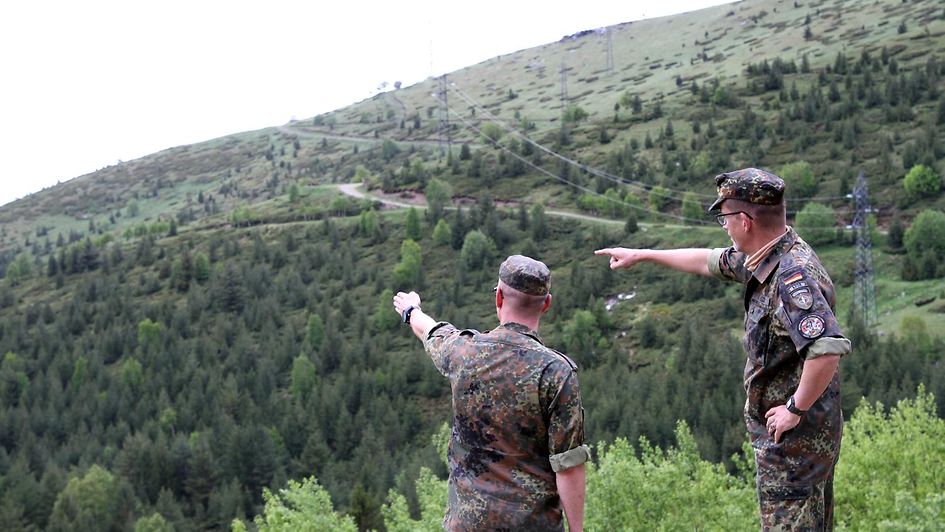 Zwei Soldaten stehen in einer Waldlandschaft.
