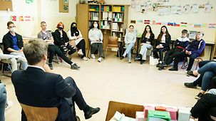 Schülerinnen und Schüler sitzen im Stuhlkreis in einem Klassenraum.