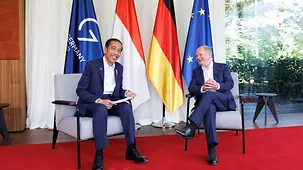 Bundeskanzler Scholz und Präsident Widodo sitzen vor Fahnen.