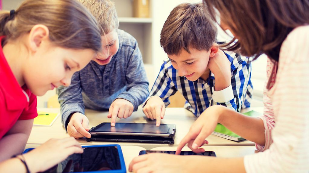 Eine Gruppe von drei Schulkindern und einer Lehrerin bedienen Tablet-PCs in einem Klassenzimmer.