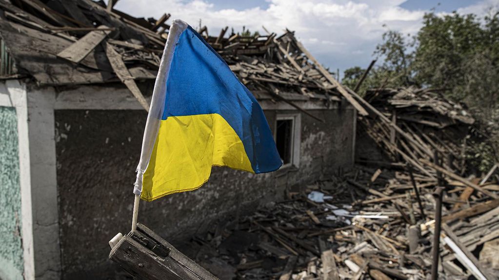 Ukrainische Flagge vor zerstörten Häusern