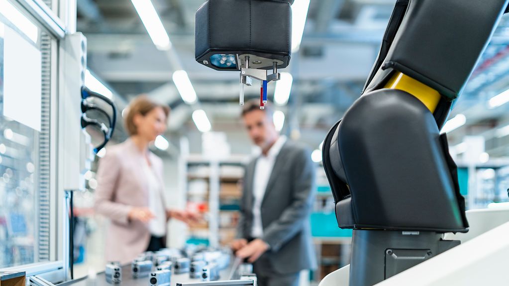 Das Bild zeigt Menschen in einer modernen Fabrik, wo Robotik eingesetzt wird.