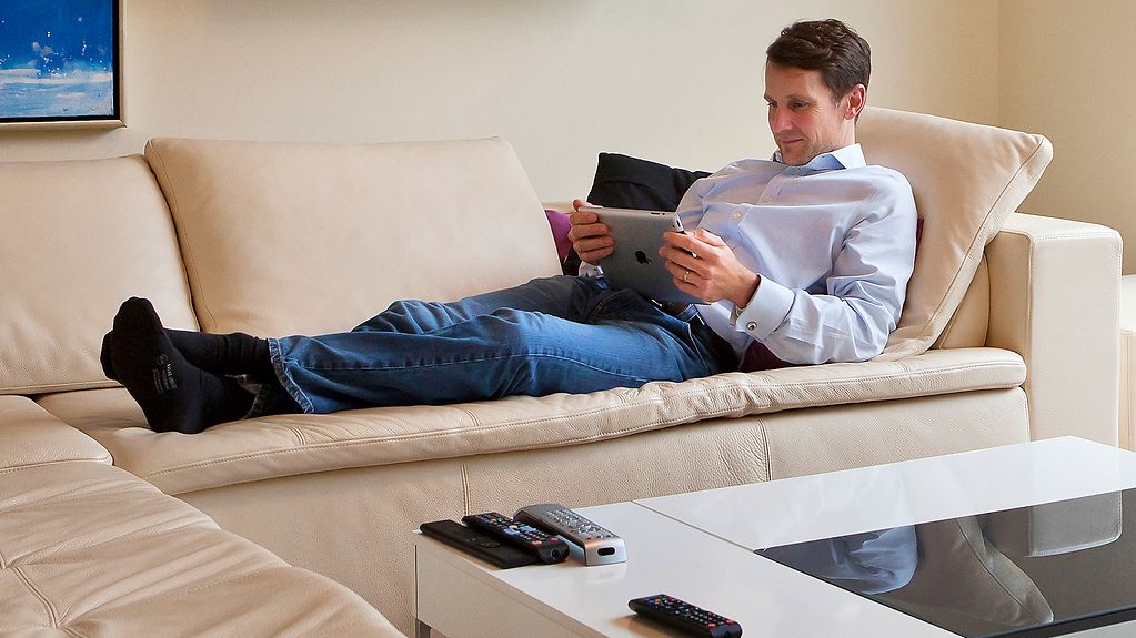 Mann liegt mit seinem Tablet auf dem Sofa. 