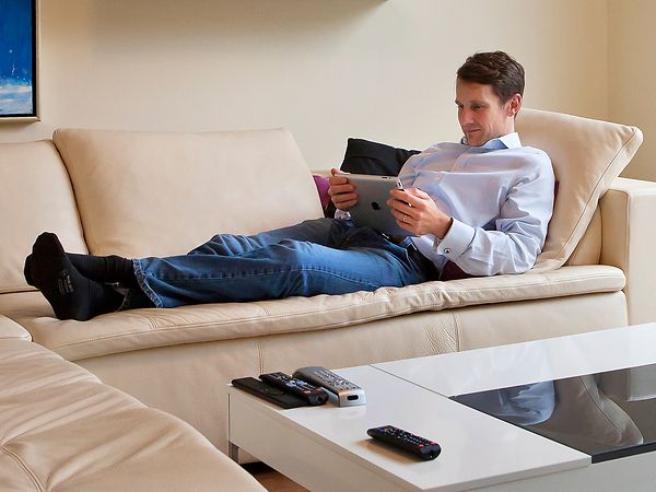 Mann liegt mit seinem Tablet auf dem Sofa. 