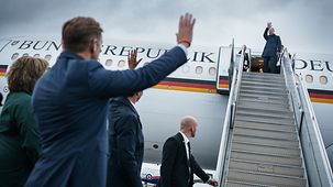 Bundeskanzler Olaf Scholz winkt aus dem Flugzeug.