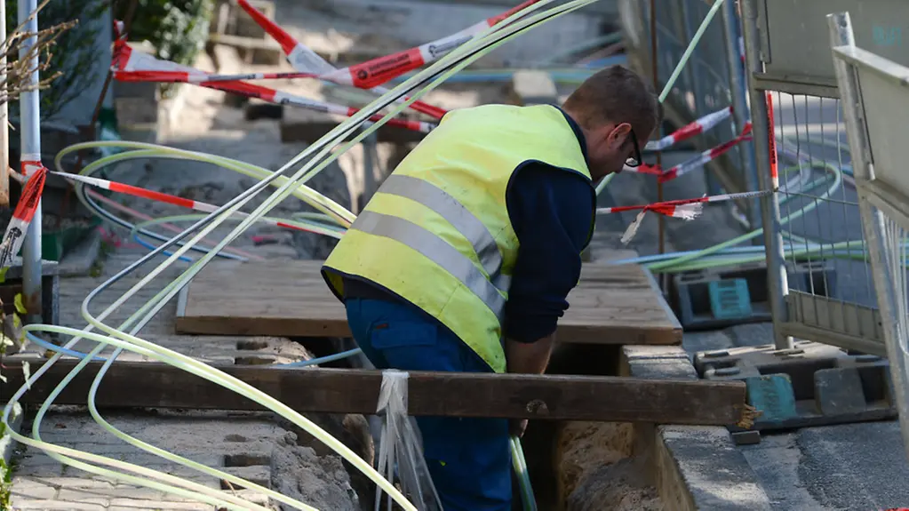 Strommonteur verlegt auf einer Baustelle Speed-Pipe-Röhrchen für Glasfasernetze und Stromkabel.