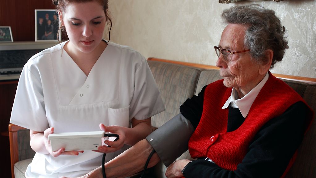 Eine Krankenschwester misst den Blutdruckt einer älteren Frau zu Hause.