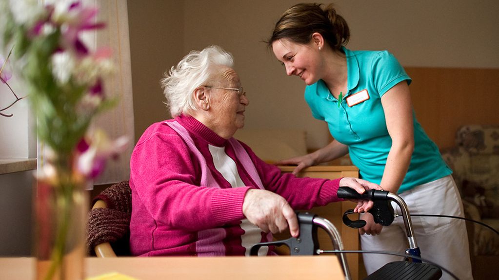 Eine Pflegerin (rechts) kümmert sich um eine Seniorin (links).