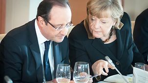 Merkel und Hollande betrachten die Münze.