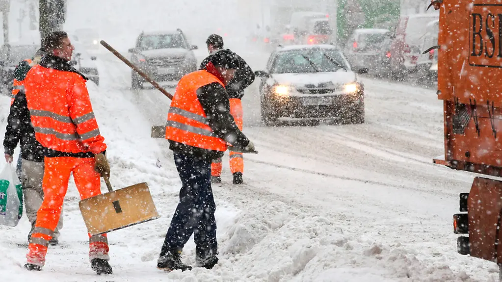 Mitarbeiter der Stadtreinigung beseitigen, bei Schneefall und Temperaturen um Minus zehn Grad Celsius, an Fußgängerübergängen den Schnee.