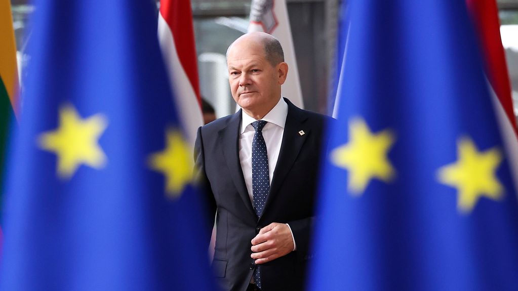 Le chancelier fédéral Olaf Scholz marchant entre deux drapeaux européens