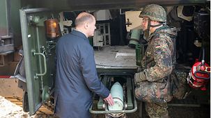 Federal Chancellor Olaf Scholz with a soldier explaining how to use a self-propelled howitzer.