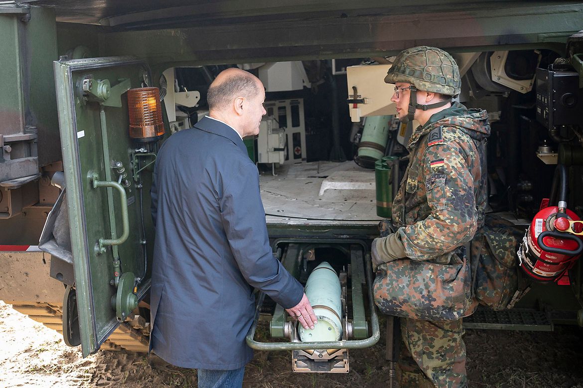 Federal Chancellor Olaf Scholz with a soldier explaining how to use a self-propelled howitzer.