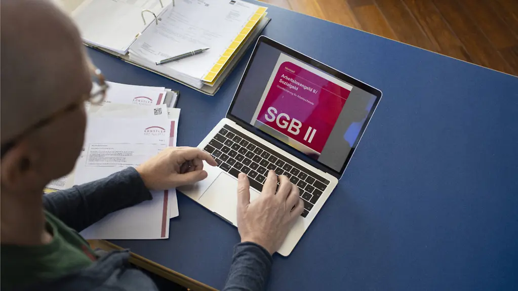 Sachbearbeiter sitzt am Laptop auf dessem Bildschirm steht SGB II.