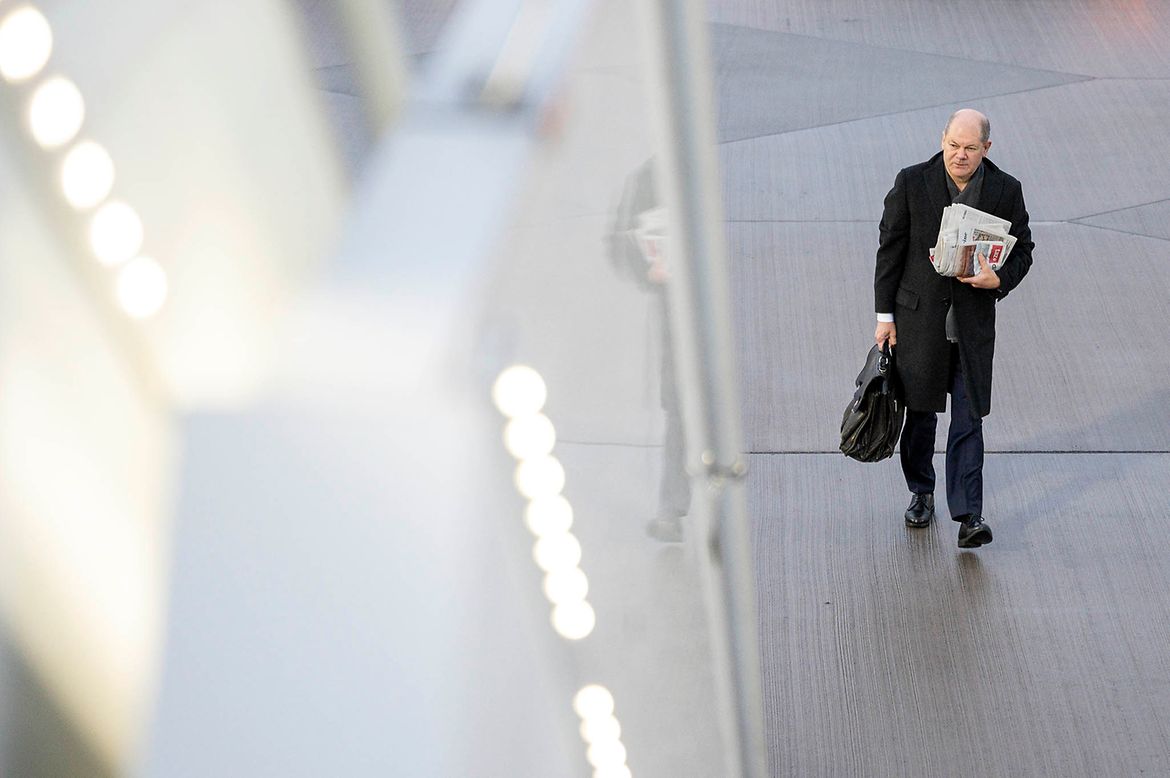 Bundeskanzler Olaf Scholz geht auf dem Flughafen mit einem Pack Zeitungen unter dem Arm zum Flugzeug.
