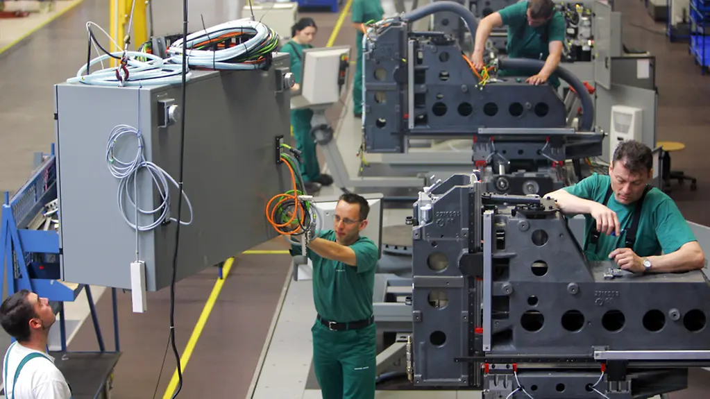 Mit Hilfe eines Krans wird ein Schaltschrank einer CNC-Universal-Fräsmaschine in einer Montagehalle angeliefert