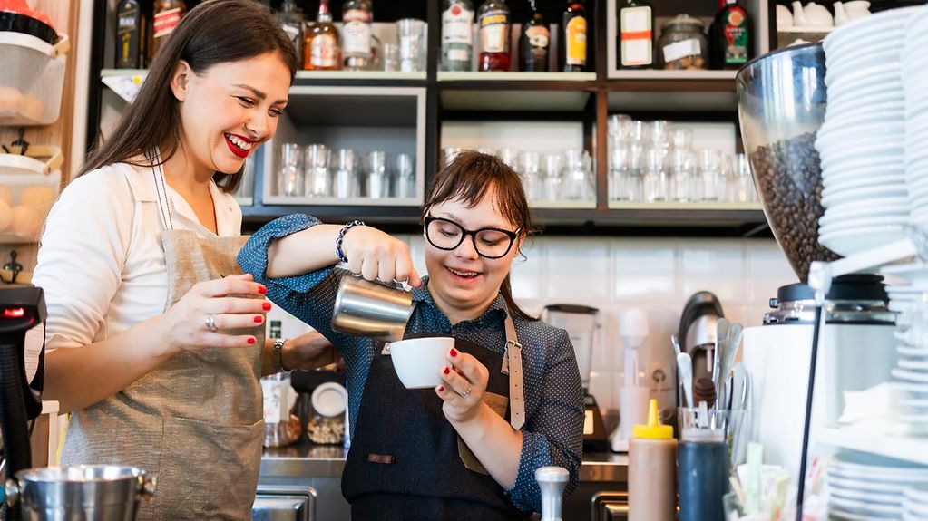 Eine junge Frau mit Down-Syndrom arbeitet in einem Café.