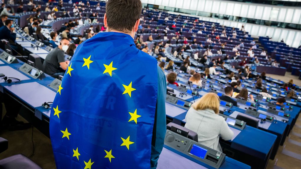 European Youth Event (EYE 2021) - Jugendlicher steht im hinteren Bereich des Plenarsaals mit einer EU-Flagge