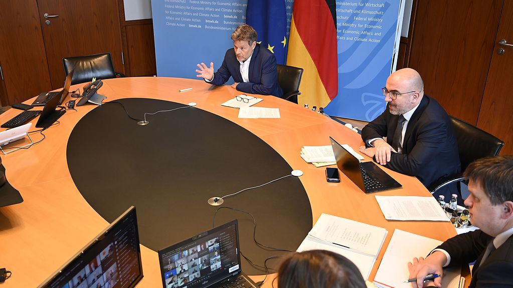 Bundesminister Robert Habeck und weitere Personen sitzen an einem Konferentisch. Sie nehmen an einer virtuellen Konferenz teil. 