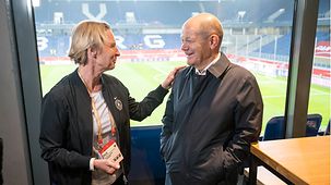 Bundeskanzler Olaf Scholz bei einem Frauenfußballspiel im Gespräch mit Bundestrainerin Martina Voss-Tecklenburg.