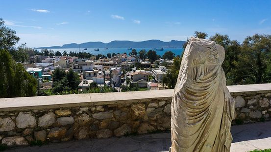 Blick von der archäologischen Stätte von Eleusis auf die Stadt Elefsina, vorne eine kopflose Statue.