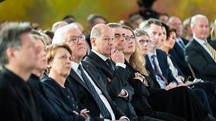 Bundeskanzler Scholz sitzt neben Bundespräsident Steinmeier in der ersten Reihe der Veranstaltung.