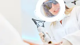Kosmetikerin mit Vergrößerungsglas bei Haarentfernung durch Alexandritlaser Epilation