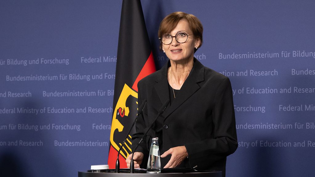 Bundesministerin Stark-Watzinger an einem Rednerpult vor der Deutschlandfahne im Bundesministerium für Bildung und Forschung.