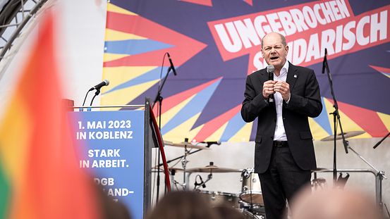 Bundeskanzler Scholz auf einer Bühne. Hinter ihm das Motte der Kundgebung: ungebrochen solidarisch.