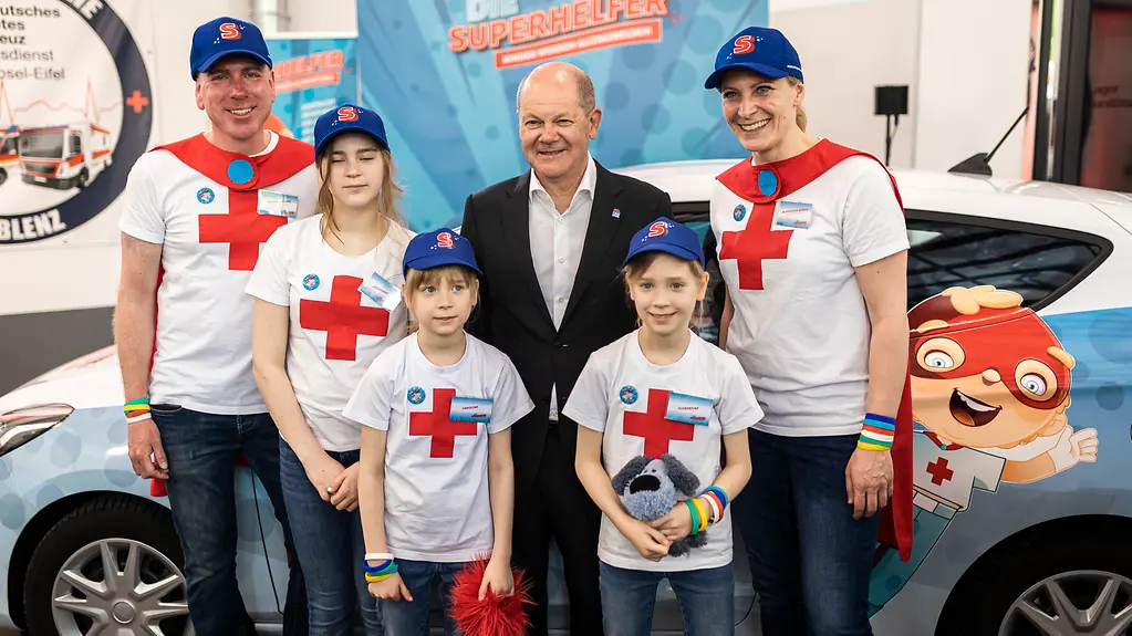 Bundeskanzler Schol mit zwei Erwachsenen und drei Kindern im Superhelfer-Outfit.
