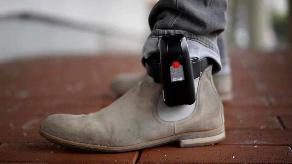 Ein Mitarbeiter der hessischen Justiz veranschaulicht, wie eine elektronische Fußfessel getragen wird.