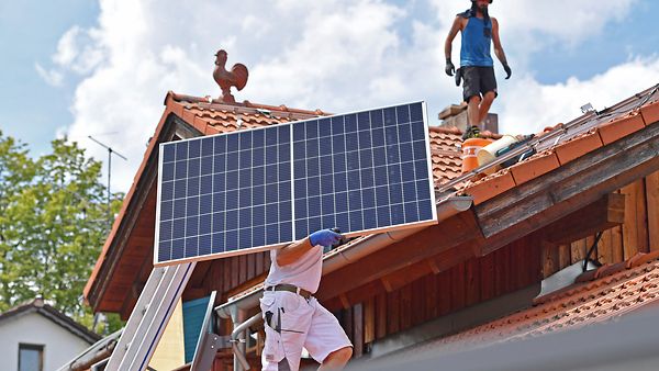 Solarmodule werden auf ein Hausdach transportiert. Ein Arbeiter traegt ein Solarpane