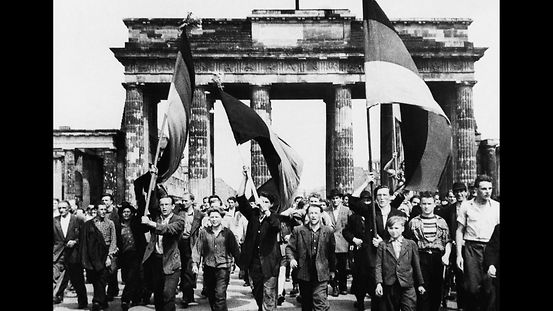 Demonstranten (mit Fahnen) gehen durchs Brandenburger Tor.